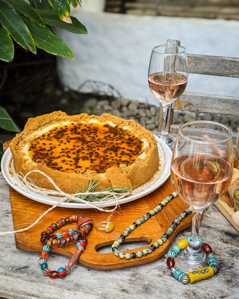 Cheesecake de maracuyá, vino rosado y joyería artesanal sobre una mesa de madera
