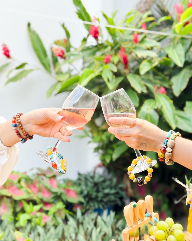 Primer plano de un brindis con copas de vino rosado y pulseras artesanales